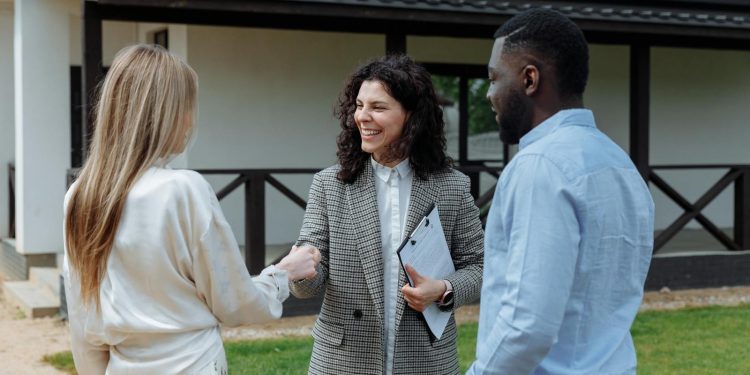 A real estate agent shakes hands with a couple outside a modern house, symbolizing a successful property deal.